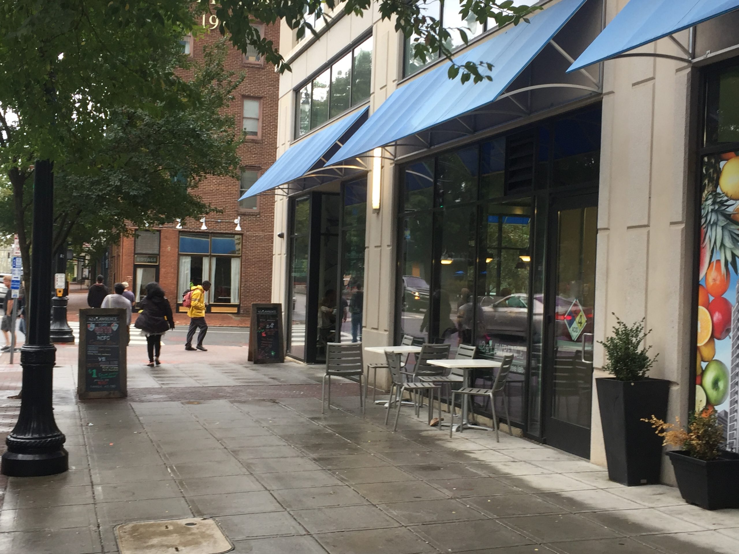 An exterior view of two small tables and chairs on the sidewalk. There are no planters or anything separating them from the rest of the sidewalk